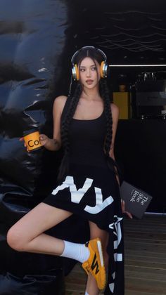 Woman with long braids and headphones holding a coffee cup and a book