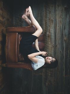 Woman in a black dress lying on a brown armchair with her feet up against a wooden wall