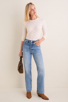 Woman with blonde hair wearing jeans and a knitted top, holding a brown handbag