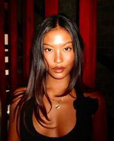 Woman with long black hair wearing a black top and necklace indoors
