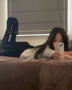 Person in a white t-shirt and black skirt taking a mirror selfie while lying on a bed