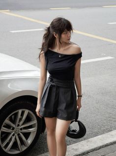 Woman in an off-shoulder top and pinstripe shorts standing next to a car