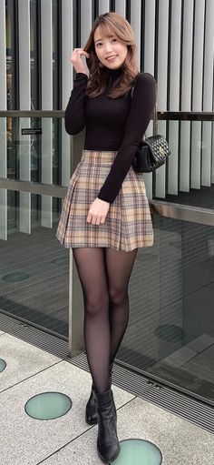 Woman in a black top and plaid skirt posing outdoors