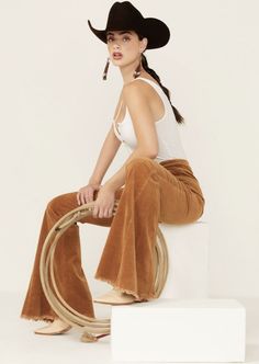 Woman in a cowboy hat and bell bottom pants holding a rope in a studio