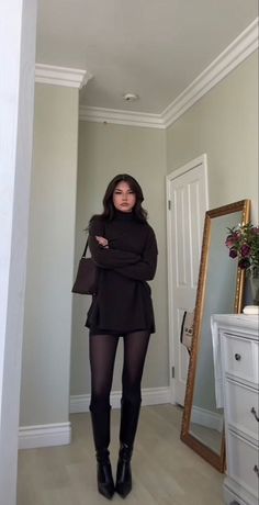 Woman in a dark turtleneck sweater and black tights standing indoors