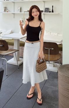 Woman in a black camisole and polka dot skirt holding a drink and bag