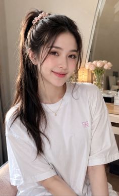 Woman with a ponytail wearing a white t-shirt and gold necklace indoors