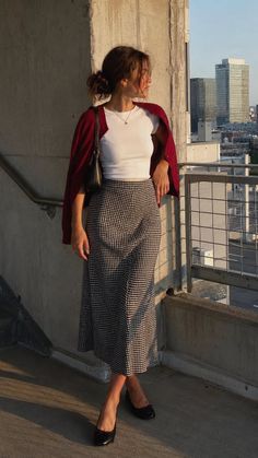 Woman in a gingham skirt and red cardigan on a rooftop at golden hour