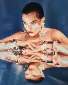 Woman with slicked back hair and clear jewelry reflected on a surface