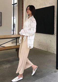 Woman in a plaid shirt and pleated pants walking indoors
