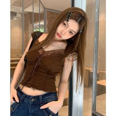 Woman with long brown hair wearing a brown lace-trimmed top and denim jeans indoors