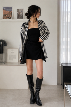 Woman in a black dress and striped shirt with knee-high boots indoors