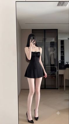 Woman in a black dress and high heels taking a mirror selfie indoors