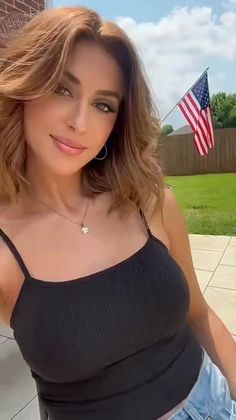 Woman with medium brown hair wearing a black tank top outdoors with an American flag