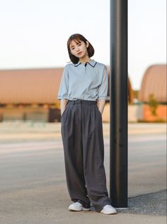 Woman with short hair wearing a polo shirt and wide leg pants outdoors