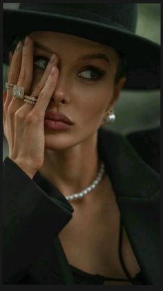 Woman in a black hat and pearl necklace, covering part of her face with her hand