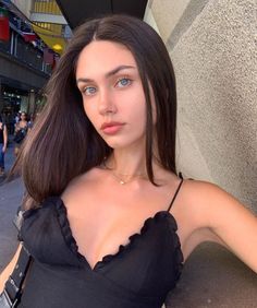 Woman with long dark hair and blue eyes wearing a black top and necklace outdoors
