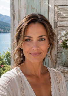Woman with long hair and earrings smiling outdoors with a lake in the background