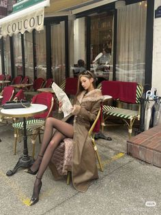 Woman in a long fur-collared coat and black tights sitting at an outdoor cafe