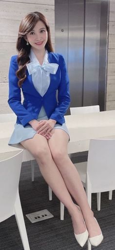 Woman in a blue blazer and light blue skirt sitting on a table indoors