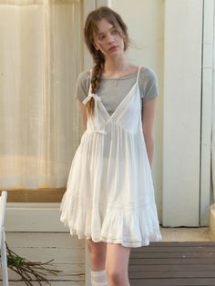 Young woman in a white dress and gray t-shirt with a long braid indoors