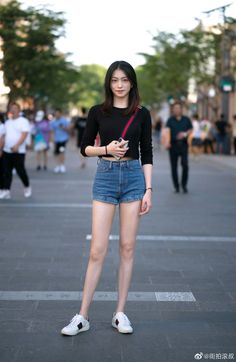 Woman in a black long-sleeve crop top and denim shorts on a street