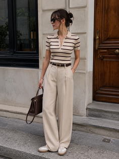 Woman in a striped polo shirt and wide leg pants holding a brown handbag