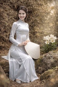 Woman in a white ao dai and conical hat sitting outdoors with white flowers