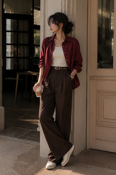 Woman in a red shirt and brown pants holding a coffee cup outdoors
