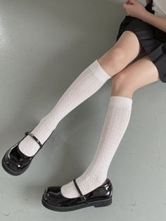 Person wearing white patterned socks and black mary jane shoes with a black skirt