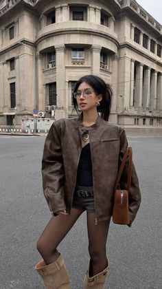 Woman in a brown leather jacket, shorts, and boots on a city street
