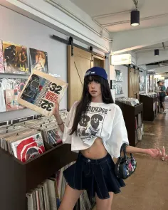 Woman in a crop top and denim skirt holding a record in a record store