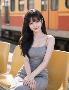 Woman with long black hair in a gray dress sitting at a train station