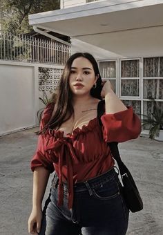 Woman in a red top and dark jeans posing outdoors