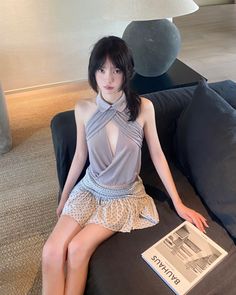 Woman with black hair wearing a halter top and mini skirt, sitting on a couch