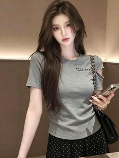 Woman with long hair wearing a gray t-shirt and polka dot skirt, holding a phone