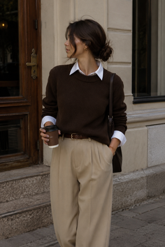 Woman in a brown sweater and beige pants holding a coffee cup outdoors