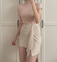 Person in a light pink turtleneck top and an asymmetrical beige mini skirt