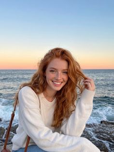Smiling woman with red hair and freckles by the ocean at sunset