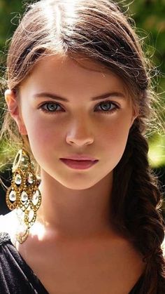 Close-up portrait of a young girl with braided hair and large earrings outdoors