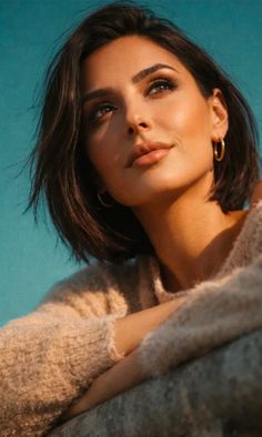 Woman with short dark hair and hoop earrings looking up against a blue background