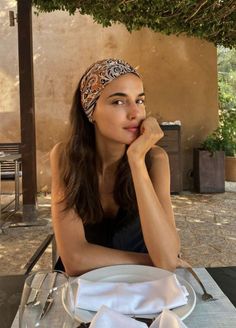 Woman with a patterned headband and long hair sitting outdoors at a table