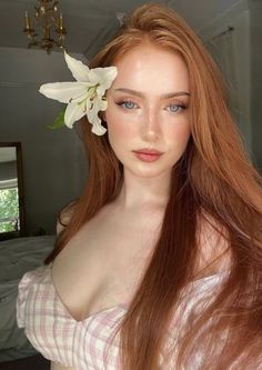 Woman with long red hair and a white lily in her hair, wearing a plaid top
