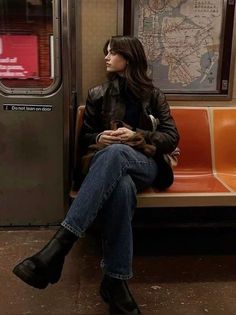 Woman with long hair in a leather jacket and jeans sitting in a subway car
