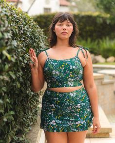 Woman in a floral print two-piece swimsuit standing next to a green hedge