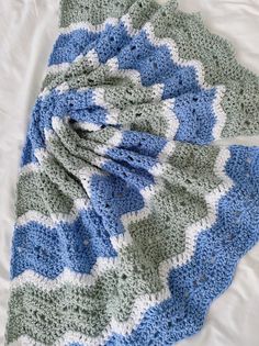 Crochet blanket with blue, green, and white chevron pattern on a white surface