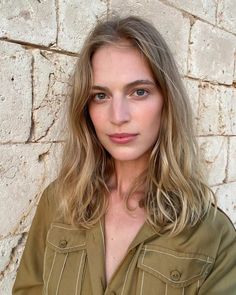Woman with blonde hair in an olive shirt against a stone wall