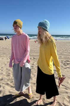 Two people in beanies and striped shirts standing on a sandy beach