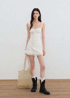 Woman in a white dress and black boots holding a mesh bag indoors