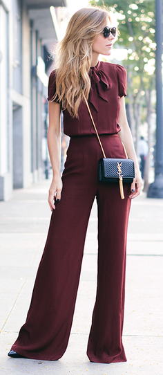 Woman in a maroon jumpsuit and sunglasses standing on a sidewalk